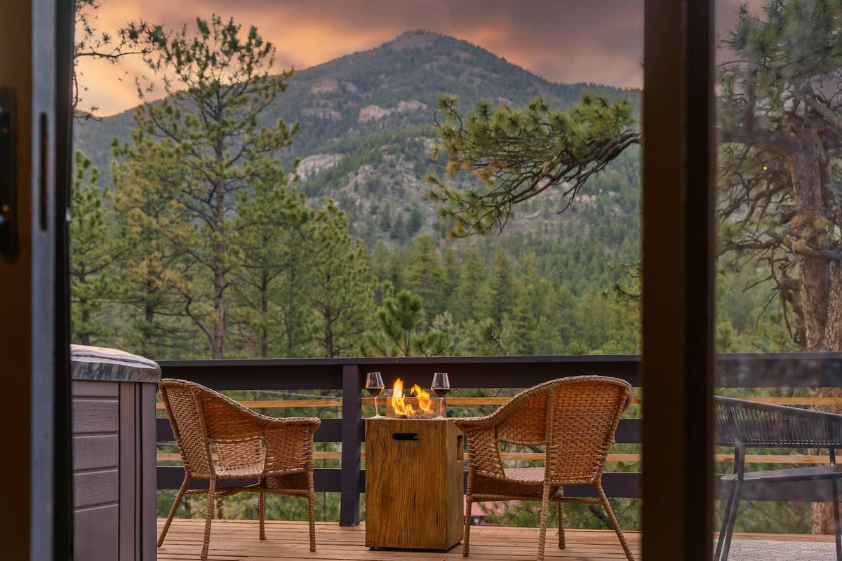 Balcony with a fire table facing a pine-covered peak at sunset at the Elegant A-Frame